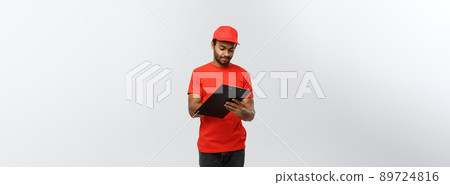 Delivery Concept - Portrait of Handsome African American delivery man or courier writing on a order document. Isolated on Grey studio Background. Copy Space. Delivery Concept - Portrait of Handsome African American delivery man or courier writing on a order document. Isolated on Grey studio Background. Copy Space. 89724816