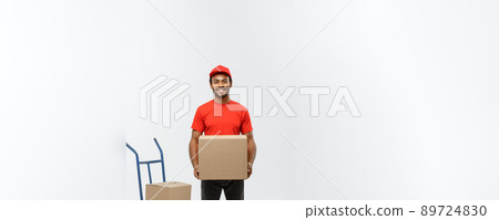 Delivery Concept - Portrait of Handsome African American delivery man or courier with hand truck and holding box. Isolated on Grey studio Background. Copy Space. 89724830