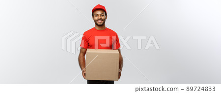 Delivery Concept - Portrait of Happy African American delivery man in red cloth holding a box package. Isolated on Grey studio Background. Copy Space. 89724833