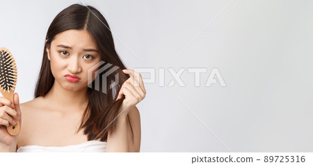 Upset stressed young Asian woman holding damaged dry hair on hands over white isolated background. 89725316