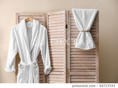 Soft comfortable bathrobe hanging on folding screen in stylish room interior 89725593