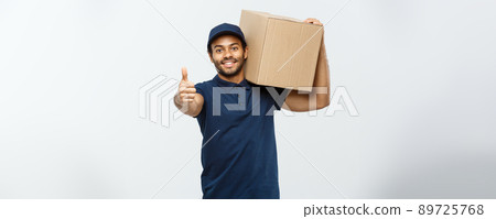 Delivery Concept - Portrait of Happy African American delivery man holding a box package and showing thumps up. Isolated on Grey studio Background. Copy Space. 89725768