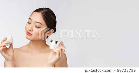Beautiful young woman on white isolated background holding cosmetic face cream, asian Beautiful young woman on white isolated background holding cosmetic face cream, asian 89725782