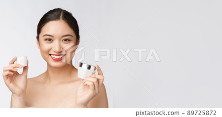 Beautiful young woman on white isolated background holding cosmetic face cream, asian 89725872