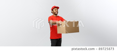Delivery Concept - Portrait of Happy African American delivery man in red cloth holding a box package. Isolated on Grey studio Background. Copy Space. Delivery Concept - Portrait of Happy African American delivery man in red cloth holding a box package. Isolated on Grey studio Background. Copy Space. 89725873