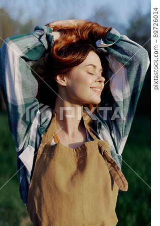 Portrait of a woman with a beautiful smile in her work clothes and apron in nature, enjoying relaxation after work in the sunset sunlight 89726014