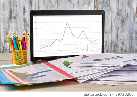 Laptop with statistic graphs and work papers with pens. 89726203