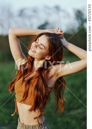 A woman warms up and stretches her arms up in nature in a green park after an outdoor sports workout in the sunset sunlight. The concept of a healthy lifestyle and an athletic body A woman warms up and stretches her arms up in nature in a green park after an outdoor sports workout in the sunset sunlight. The concept of a healthy lifestyle and an athletic body 89726530