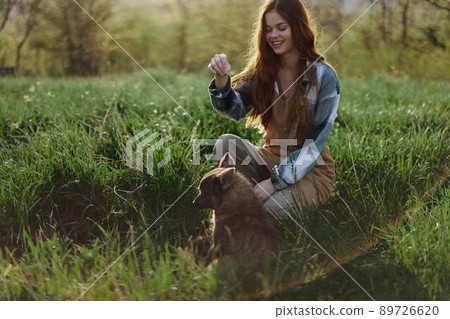 Young redheaded woman playing in nature with her dog in sunny park at sunset in summer Young redheaded woman playing in nature with her dog in sunny park at sunset in summer 89726620