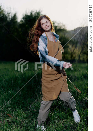 Woman farm worker in apron relaxing in nature and watching the sunset after a day of work on the farm Woman farm worker in apron relaxing in nature and watching the sunset after a day of work on the farm 89726715