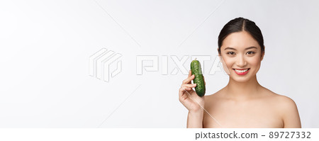 Asian young woman over isolated background holding cucumber. Asian young woman over isolated background holding cucumber. 89727332