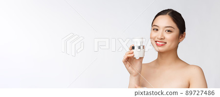Beautiful young woman on white isolated background holding cosmetic face cream, asian 89727486