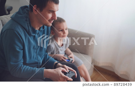 Happy father and son sit in the living room on the sofa and play or watch TV Happy father and son sit in the living room on the sofa and play or watch TV 89728439