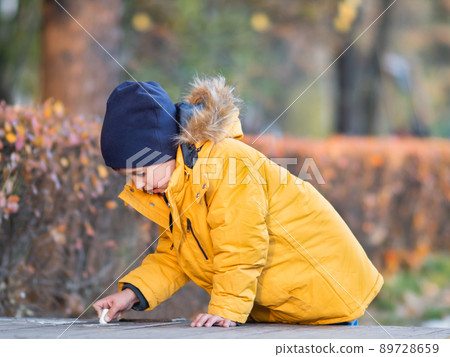 Little boy writes or draws something with chalk on pavement. Creative leisure activity outdoors at fall. 89728659