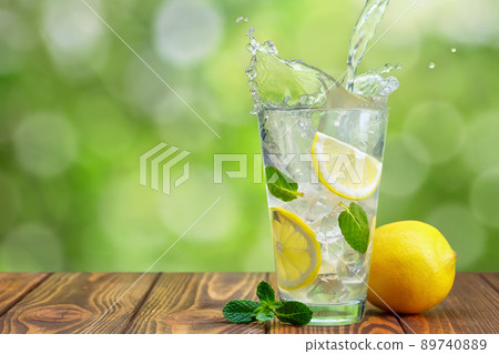 lemonade pouring in glass on wooden table with green blurred background 89740889