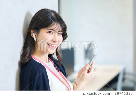 A woman leaning against a wall and holding a smartphone 89745353