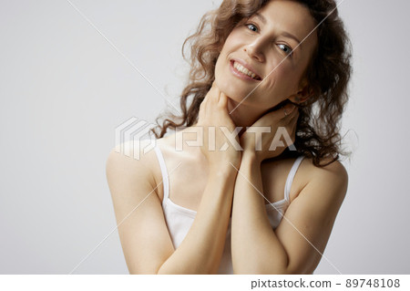 Joyful awesome curly beautiful woman in basic white t-shirt touches neck smiles at camera posing isolated on over white background. People Emotions Lifestyle concept. Copy space 89748108