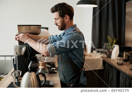 Barista pours coffee beans into the coffee machine tank for grinding at coffeeshop Barista pours coffee beans into the coffee machine tank for grinding at coffeeshop 89748374