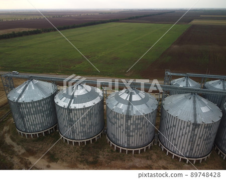 Grain elevator. Metal grain elevator in agricultural zone. Agriculture storage for harvest. Grain elevators on green nature background. Exterior of agricultural factory. Nobody. 89748428