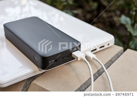 Power bank charges a laptop via USB type C cable on the street. Close-up, selective focus Power bank charges a laptop via USB type C cable on the street. Close-up, selective focus 89748971
