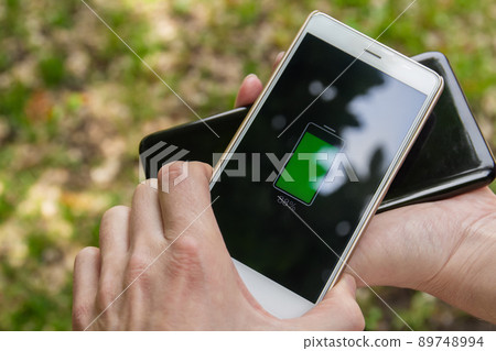 Phone battery wireless charge sharing technology. People share their smartphone charge by wireless in the park. 89748994