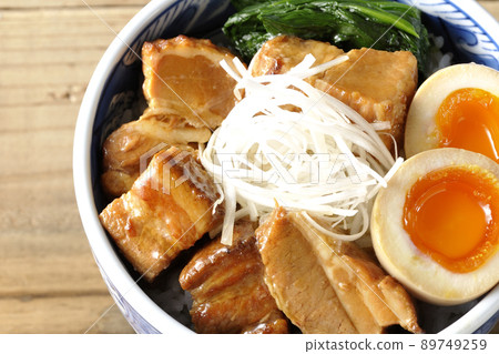 A bird's-eye view of a pork kakuni bowl with a soft-boiled egg, spinach, and white onions. 89749259