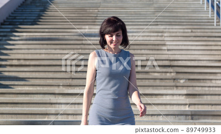 Happy woman in summer dress quickly runs up the steps to the beach Happy woman in summer dress quickly runs up the steps to the beach 89749933