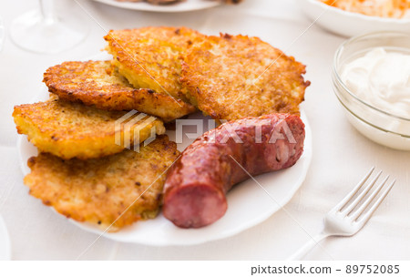 Fried grated potato pancakes with fried sausage on white plate 89752085