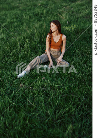 Freelancer woman enjoying the outdoors sitting in the park on the green grass in casual clothing with long red hair lit by the bright summer sun without mosquitoes Freelancer woman enjoying the outdoors sitting in the park on the green grass in casual clothing with long red hair lit by the bright summer sun without mosquitoes 89752849