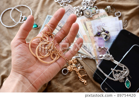 Marauders hand with bunch of stolen jewelry, money and smartphones on military uniform cloth fabric. Looting by Russian soldiers in the Ukrainian cities during Russian invasion on Ukraine Marauders hand with bunch of stolen jewelry, money and smartphones on military uniform cloth fabric. Looting by Russian soldiers in the Ukrainian cities during Russian invasion on Ukraine 89754420