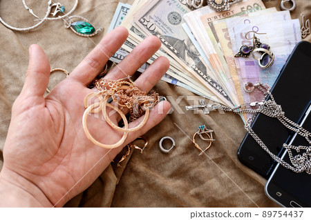 Marauders hand with bunch of stolen jewelry, money and smartphones on military uniform cloth fabric. Looting by Russian soldiers in the Ukrainian cities during Russian invasion on Ukraine Marauders hand with bunch of stolen jewelry, money and smartphones on military uniform cloth fabric. Looting by Russian soldiers in the Ukrainian cities during Russian invasion on Ukraine 89754437