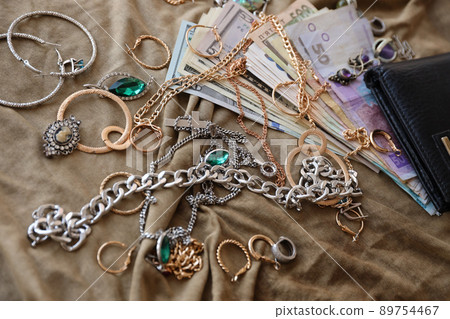 Bunch of stolen jewelry and money on military uniform cloth fabric. Looting by Russian soldiers in the Ukrainian cities during the Russian attack on Ukraine. Marauders and looters Bunch of stolen jewelry and money on military uniform cloth fabric. Looting by Russian soldiers in the Ukrainian cities during the Russian attack on Ukraine. Marauders and looters 89754467