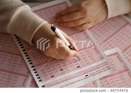 Filling out a lottery ticket. A young woman plays the lottery and dreams of winning the jackpot. Female hand marking number on red lottery ticket 89754478