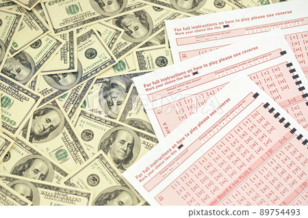 Pink gambling sheets with numbers for marking on big amount of hundred dollar bills. Lottery playing concept or gambling addiction. Close up Pink gambling sheets with numbers for marking on big amount of hundred dollar bills. Lottery playing concept or gambling addiction. Close up 89754493