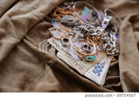 Bunch of stolen jewelry and money on military uniform cloth fabric. Looting by Russian soldiers in the Ukrainian cities during the Russian attack on Ukraine. Marauders and looters Bunch of stolen jewelry and money on military uniform cloth fabric. Looting by Russian soldiers in the Ukrainian cities during the Russian attack on Ukraine. Marauders and looters 89754507