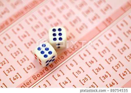 Dice cubes lies on pink gambling sheets with numbers for marking to play lottery. Lottery playing concept or gambling addiction. Close up Dice cubes lies on pink gambling sheets with numbers for marking to play lottery. Lottery playing concept or gambling addiction. Close up 89754535
