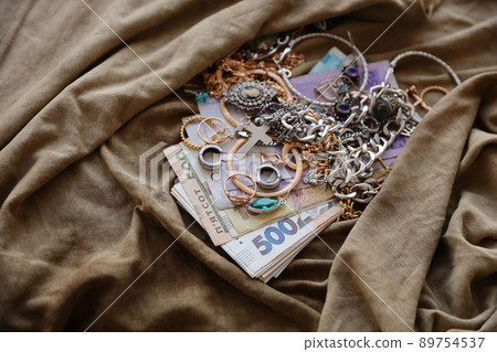 Bunch of stolen jewelry and money on military uniform cloth fabric. Looting by Russian soldiers in the Ukrainian cities during the Russian attack on Ukraine. Marauders and looters Bunch of stolen jewelry and money on military uniform cloth fabric. Looting by Russian soldiers in the Ukrainian cities during the Russian attack on Ukraine. Marauders and looters 89754537