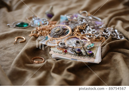 Bunch of stolen jewelry and money on military uniform cloth fabric. Looting by Russian soldiers in the Ukrainian cities during the Russian attack on Ukraine. Marauders and looters Bunch of stolen jewelry and money on military uniform cloth fabric. Looting by Russian soldiers in the Ukrainian cities during the Russian attack on Ukraine. Marauders and looters 89754567