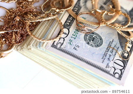 Many expensive golden jewerly rings, earrings and necklaces with big amount of US dollar bills on white background. Pawnshop or jewerly shop 89754611