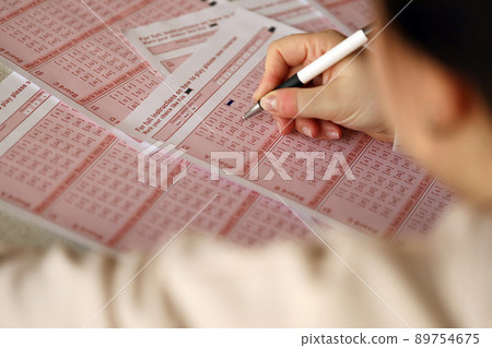 Filling out a lottery ticket. A young woman plays the lottery and dreams of winning the jackpot. Female hand marking number on red lottery ticket Filling out a lottery ticket. A young woman plays the lottery and dreams of winning the jackpot. Female hand marking number on red lottery ticket 89754675