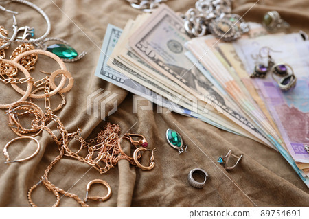 Bunch of stolen jewelry and money on military uniform cloth fabric. Looting by Russian soldiers in the Ukrainian cities during the Russian attack on Ukraine. Marauders and looters Bunch of stolen jewelry and money on military uniform cloth fabric. Looting by Russian soldiers in the Ukrainian cities during the Russian attack on Ukraine. Marauders and looters 89754691