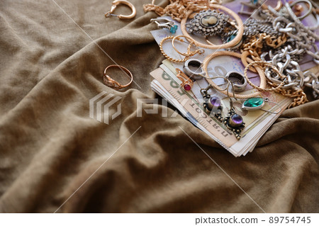 Bunch of stolen jewelry and money on military uniform cloth fabric. Looting by Russian soldiers in the Ukrainian cities during the Russian attack on Ukraine. Marauders and looters Bunch of stolen jewelry and money on military uniform cloth fabric. Looting by Russian soldiers in the Ukrainian cities during the Russian attack on Ukraine. Marauders and looters 89754745