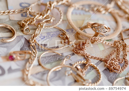 Many expensive golden jewerly rings, earrings and necklaces with big amount of Ukrainian money bills. Pawnshop or jewerly shop concept. Jewelry trading 89754974