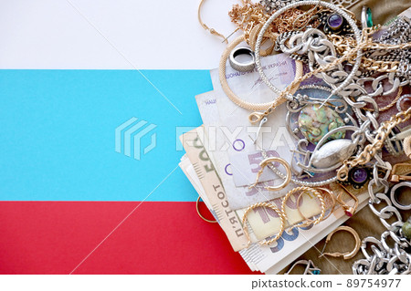 Bunch of stolen jewelry and money on military uniform cloth fabric and russian flag. Looting by Russian soldiers in the Ukrainian cities during the Russian attack on Ukraine Bunch of stolen jewelry and money on military uniform cloth fabric and russian flag. Looting by Russian soldiers in the Ukrainian cities during the Russian attack on Ukraine 89754977