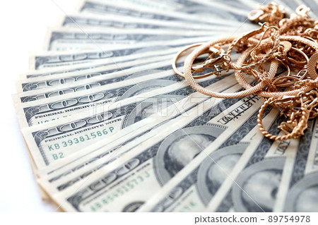Many expensive golden jewerly rings, earrings and necklaces with big amount of US dollar bills on white background. Pawnshop or jewerly shop Many expensive golden jewerly rings, earrings and necklaces with big amount of US dollar bills on white background. Pawnshop or jewerly shop 89754978
