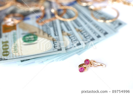 Many expensive golden jewerly rings, earrings and necklaces with big amount of US dollar bills on white background. Pawnshop or jewerly shop Many expensive golden jewerly rings, earrings and necklaces with big amount of US dollar bills on white background. Pawnshop or jewerly shop 89754996