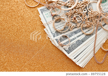 Many expensive golden jewerly rings, earrings and necklaces with big amount of US dollar bills on luxury glitter golden background surface. Pawnshop or jewerly shop Many expensive golden jewerly rings, earrings and necklaces with big amount of US dollar bills on luxury glitter golden background surface. Pawnshop or jewerly shop 89755128