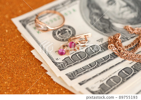 Expensive golden jewerly ring, earrings and necklace with big amount of US dollar bills on luxury glitter golden background surface. Pawnshop or jewerly shop Expensive golden jewerly ring, earrings and necklace with big amount of US dollar bills on luxury glitter golden background surface. Pawnshop or jewerly shop 89755193