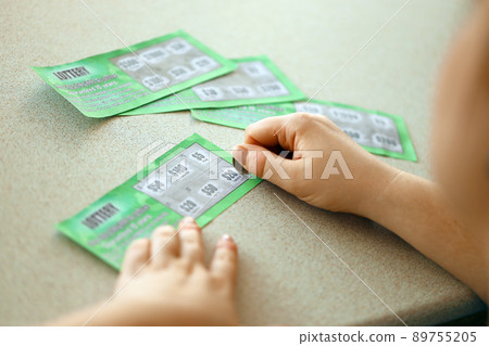Close up view of silver coin in hand of gambler scratching fake lottery card. Lottery gambling concept, scratching cards lottery 89755205