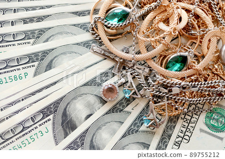 Many expensive golden and silver jewerly rings, earrings and necklaces on big amount of US dollar bills close up. Pawnshop or jewerly shop 89755212